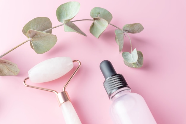 Photo beauty products facial roller cosmetic oil and serum on pink background euqalyptus leaves top view natural cosmetics and beauty treatment