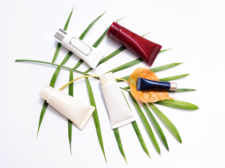 Photo beauty products with cream tube, body lotion, facial cleansing foam, cosmetics on bamboo leaves.