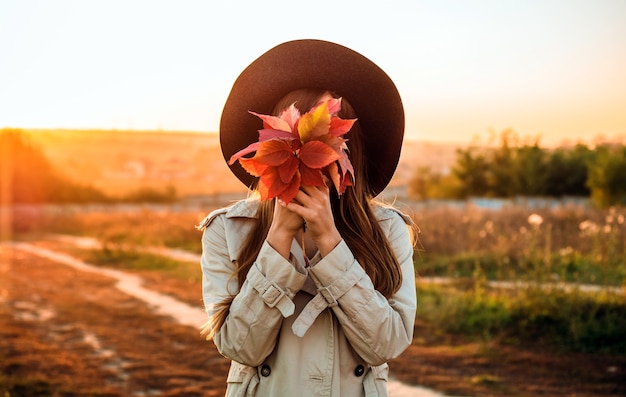 Beauty Romantic woman Outdoors enjoying nature holding leaves in hands. Beautiful autumn model with waving glow hair. Sun light on sunset. Portrait of romantic female