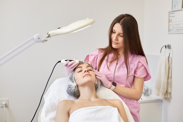 Beauty salon, doctor in pink medical gown and gloves doing dermatologic procedures