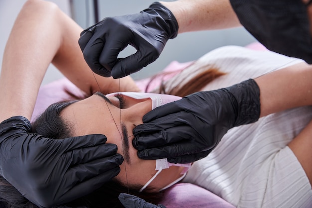 Beauty salon worker treading a clients eyebrows