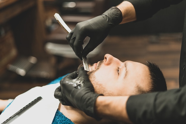 Negozio di bellezza per uomo. radersi la barba in un barbiere. il barbiere si taglia la barba con un rasoio e un tagliatore. vicino tagli di capelli brutali. attrezzature per parrucchieri. messa a fuoco selettiva.