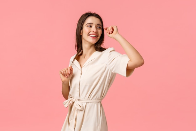 Concetto di bellezza, shopping e moda. donna castana sorridente ottimista spensierata in vestito, ballando allegramente girando a destra e sorridendo ottimista, stando rosa godendo della festa