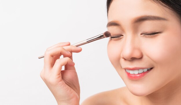 Photo beauty shot of smiley asian woman with hand holding makeup powder brush on face. cosmetic of perfect skin.