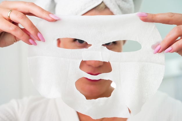 Foto concetto di bellezza per la cura della pelle bella donna caucasica che applica una maschera di carta sul viso bianco