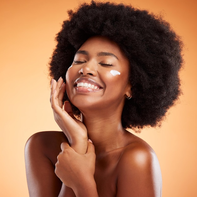 Beauty skincare and black woman with a facial product or cream on her face in studio with brown background Smile afro and happy African model with a natural lotion for glowing smooth and soft skin