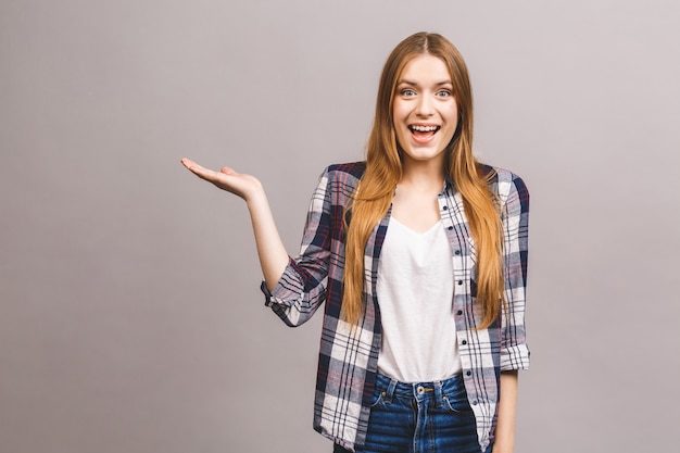 Beauty smiling young woman pointing away and looking isolated over grey wall. Free copyspace for product or text.