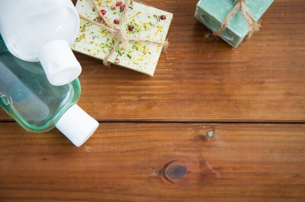 beauty, spa, body care, bath and natural cosmetics concept - close up of handmade soap bars and lotion bottles on wooden table