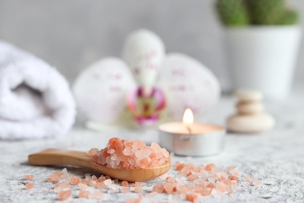 Beauty and spa concept Pink Himalayan salt on wooden spoon with candle orchid flower and towel