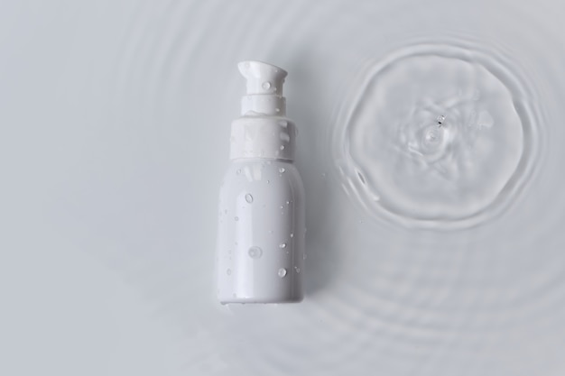 ビューティースパの医療用スキンケアと化粧品。ローションディスペンサーボトルは、ドロップ、夏の新鮮なコンセプトで白い水の背景にクリーム包装製品をモックアップします。