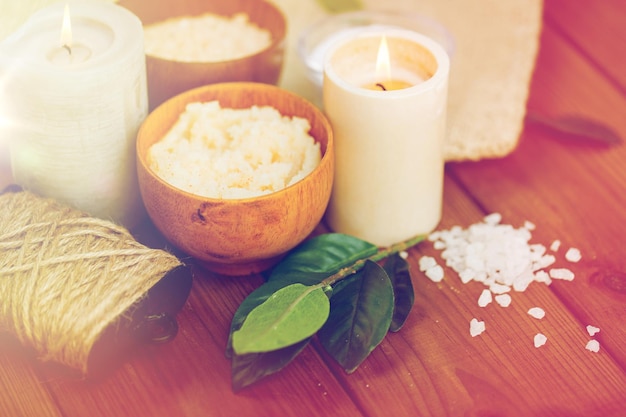 beauty, spa, therapy and natural cosmetics concept - close up of body scrub, salt and candles on wood