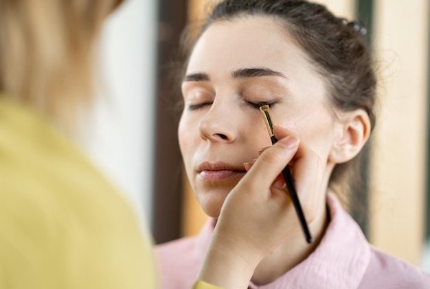 Beauty stylist applying makeup to a young model Professional Makeup artist doing glamour