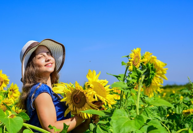 夏の自然の美しさ ヒマワリ畑の少女 ヒマワリの黄色の花 幸せな子供時代 美しい少女は、フィールドで麦わら帽子をかぶる 心に花を持つかわいい子供 自信を持って