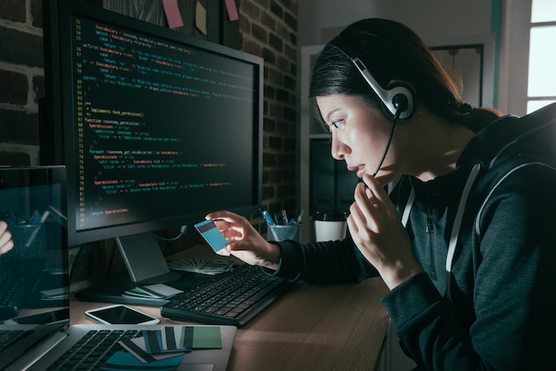 Photo beauty sweet hacker wearing headset and holding credit card doing telecommunications fraud in order to getting many money for herself.