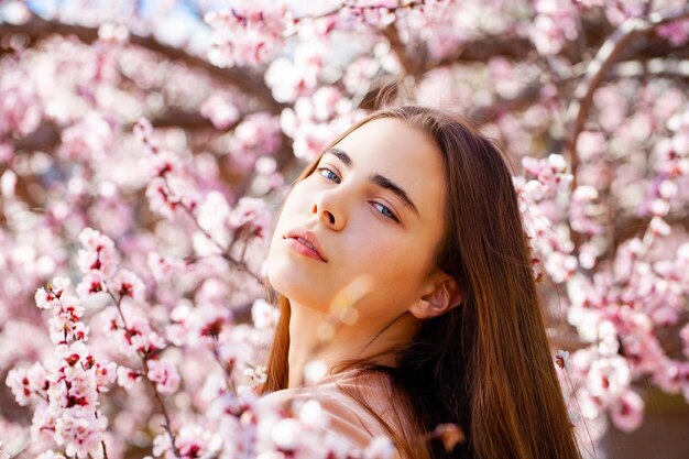 Photo beauty teen girl posing near blossom cherry tree with pink flowers spring park