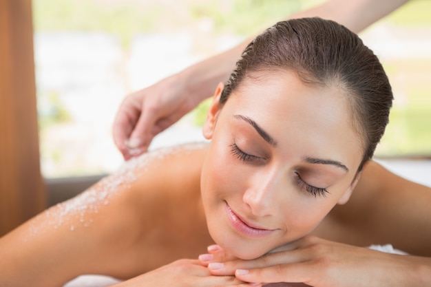 Beauty therapist pouring salt scrub on smiling womans back