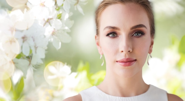 beauty, wedding and people concept - face of beautiful woman or bride in white dress over natural spring cherry blossom background