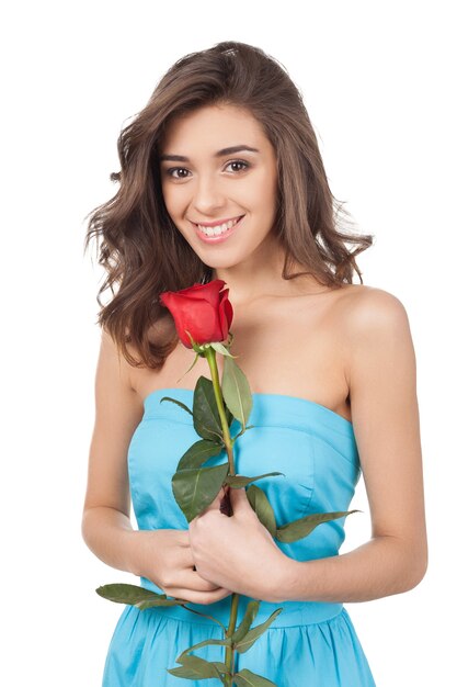 赤いバラの美しさ。赤いバラを保持し、白い背景で隔離に立っている間カメラに笑みを浮かべて美しい若い女性