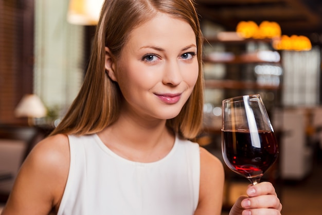 Beauty with wine. Beautiful young woman holding glass with red wine and smiling while sitting at the restaurant