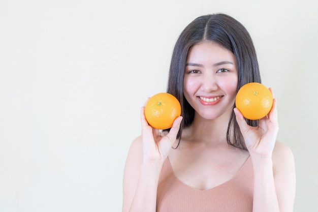 美容女性アジアのかわいい女の子は、健康ライフ スタイルのためにオレンジ色の果物を持って幸せを感じる