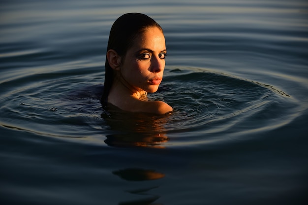 Beauty Woman face Portrait. Summer beautiful Girl. Young woman against blue water, good summer resort. Lovely fit female model on sea.