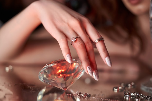 Beauty Woman holds big diamond in hand while lying on table