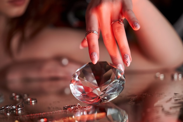 Beauty Woman houdt grote diamant in de hand terwijl ze op tafel ligt. Mooie handen, professionele manicure, grote briljant