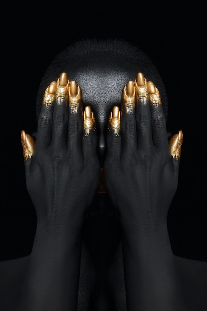 Beauty woman painted in black skin color body art gold makeup lips eyelids fingertips nails in gold color paint Professional gold makeup