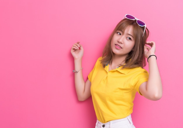 Beauty woman posing with sunglasses in front of pink wall background