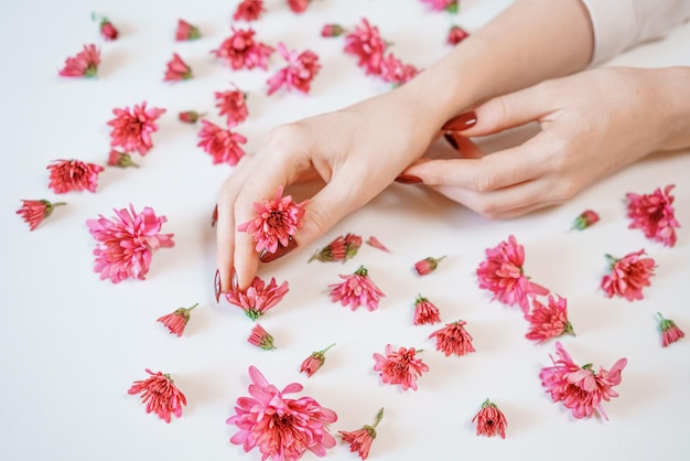 La mano della donna di bellezza con i fiori rosa si trova sullo sfondo chiaro del tavolo naturale