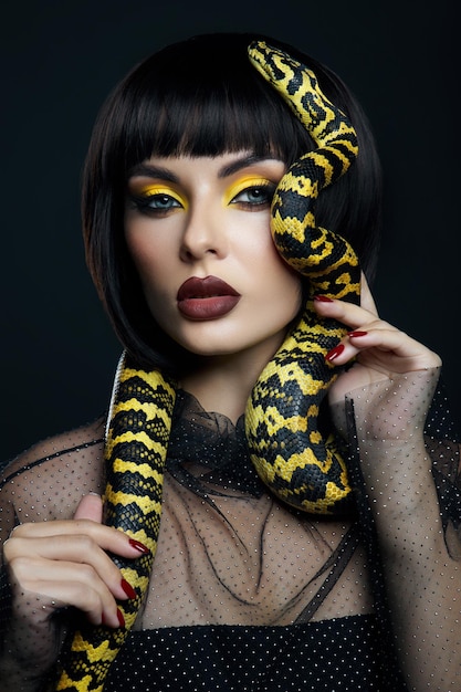 Beauty woman short haircut python yellow snake on her neck. a\
yellow snake on the shoulders of a girl. beauty yellow eye shadow\
makeup, dark burgundy lipstick