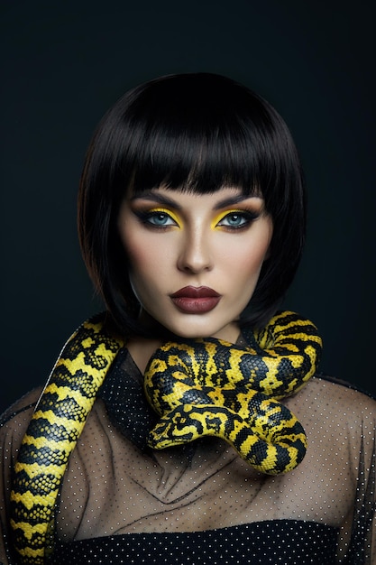 Beauty woman short haircut python yellow snake on her neck. a\
yellow snake on the shoulders of a girl. beauty yellow eye shadow\
makeup, dark burgundy lipstick