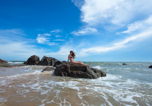 Donna di bellezza che si siede sulla roccia nell'oceano tropicale stupefacente