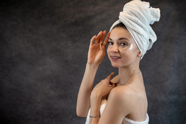 Beauty woman in towel applies black collagen patches under eyes isolated on black Skincare anti fatigue eye mask