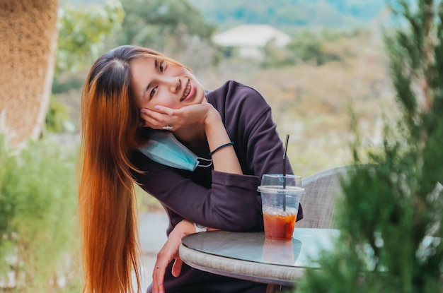 写真 美しさ若いアジアの笑顔の女性は、テーブルの上にアイスコーヒーと森の自然の背景を持つカフェに座っています