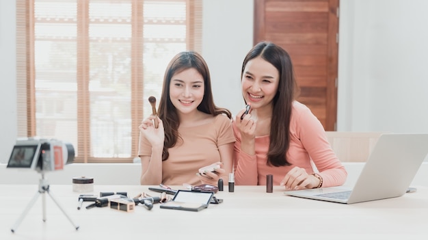 Beautybloggers, twee mooie Aziatische vrouwen proberen cosmetica te begrijpen en te verkopen. Via online streaming vanaf camera's en laptops met een blij lachend gezicht, een nieuw normaal bedrijf