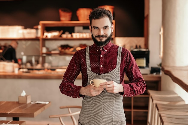 Bebaarde barista met kopje koffie in café