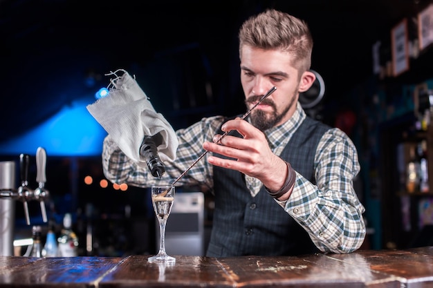 Bebaarde barkeeper die verse alcoholische drank in de glazen giet terwijl hij bij de bar in de nachtclub staat
