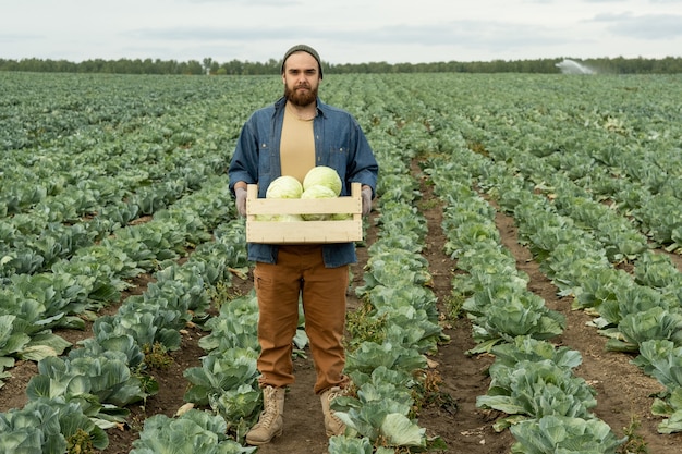 Bebaarde boer in werkkleding met doos met kolen in het veld