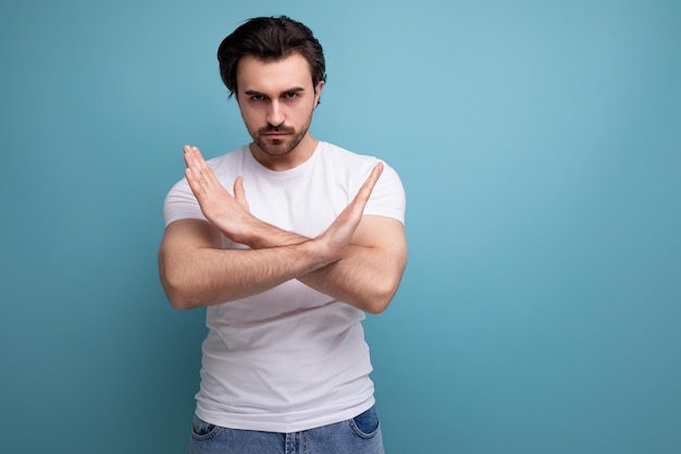 Bebaarde brunette man in witte t-shirt toont weigering gebaar op studio achtergrond met kopie ruimte