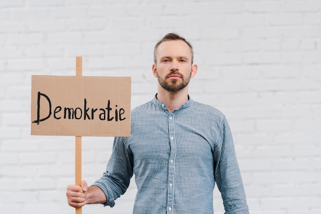 Bebaarde burger met plakkaat met democratische letters in de buurt van bakstenen muur