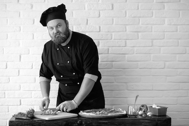 Bebaarde chef-kok bereidt maaltijden aan tafel in de keuken