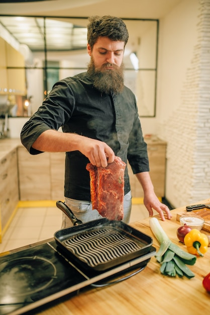 Bebaarde chef-kok koken van vlees in een pan op de keuken