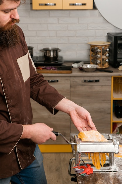 Bebaarde chef-kok met pastamachine doet geel deeg voor noedels