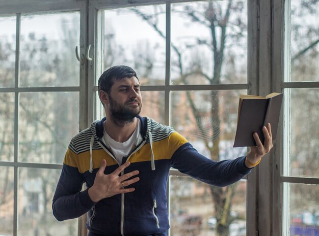 Bebaarde dichter man leest een boek met een uitdrukking. Groot raam op de achtergrond.