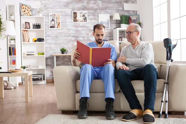 Bebaarde dokter leest een verhaal voor in een verpleeghuis voor een oude man. Oudere leeftijd man met krukken.