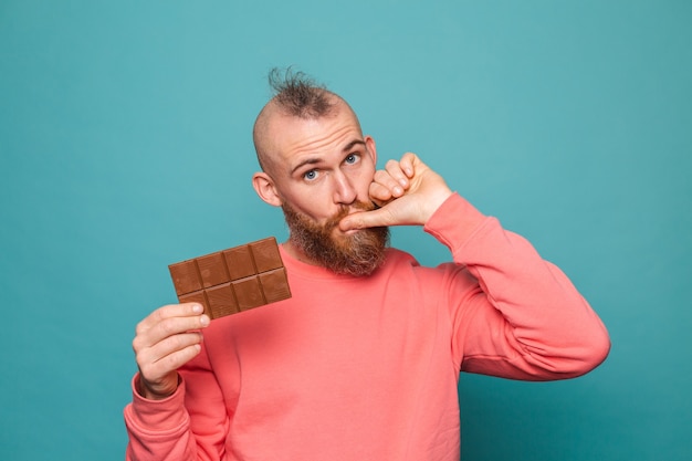 Bebaarde europese man in casual perzik geïsoleerd, met heerlijke chocolade likkende vingers