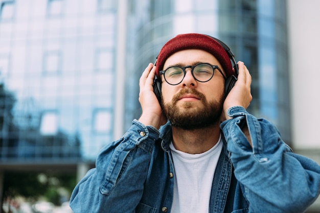 Bebaarde hipster man geniet van muziek met gesloten ogen in koptelefoon buiten in de stad. ruimte voor tekst.