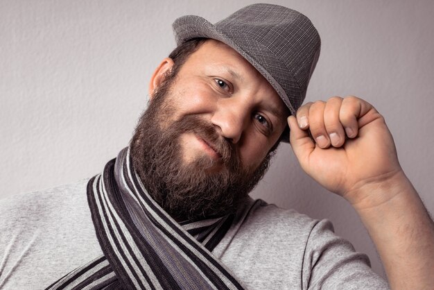 Bebaarde jonge hipster man met grijze muts en sjaal, mode portret tegen grijze muur.