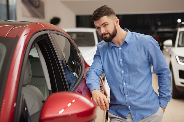 Bebaarde jonge man kijken naar een nieuwe auto dealer salon, kopie ruimte